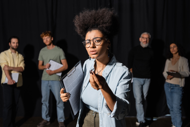 african american woman holding screenplay and gesturing during rehearsal near blurred actors and acting skills teacher - 写真・画像