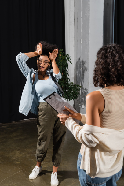 african american actress showing bunny ears with hands near multiracial woman with clipboard in theater - Фото, изображение