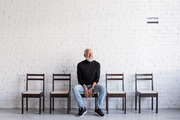 bearded man smiling with closed eyes while sitting on chair and waiting for casting - Fotoğraf, Görsel