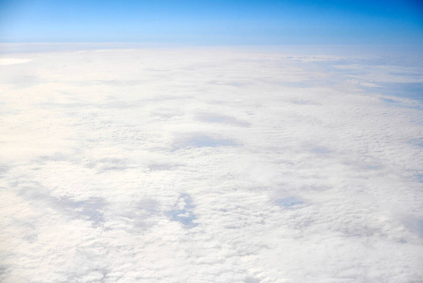 Over clouds top view from aircraft window, thick white blue clouds looks like soft foam, overcast with fresh frosty air. Beautiful cloudy sky view to troposphere, heavy cloudiness - Foto, Bild