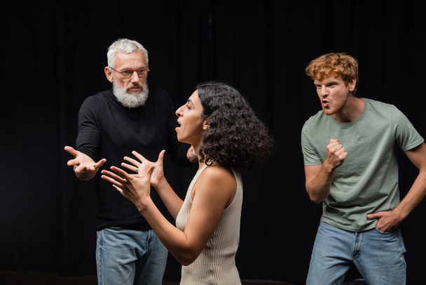 multicultural actress rehearsing near gesturing acting skills teacher and emotional redhead man in theater - Foto, imagen