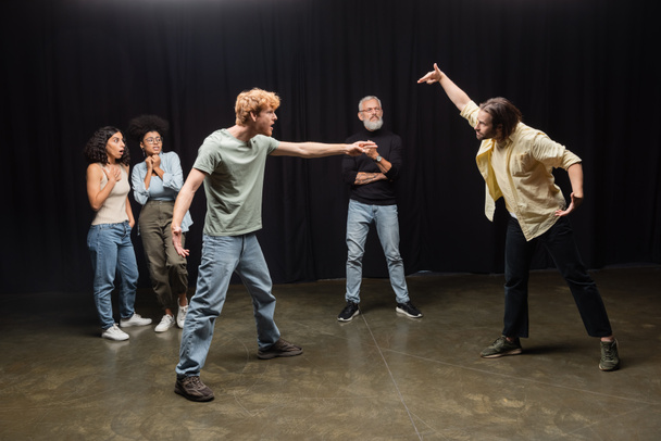 full length of young actors rehearsing near astonished interracial women and art director. Translation of tattoo: om, shanti, peace   - Fotoğraf, Görsel
