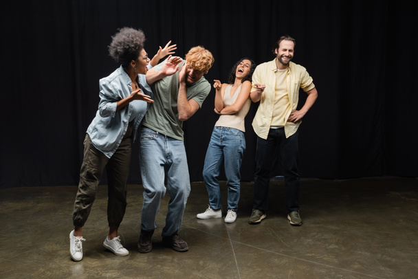 cheerful interracial actors pointing at african american woman rehearsing with redhead man on stage in theater - Фото, изображение