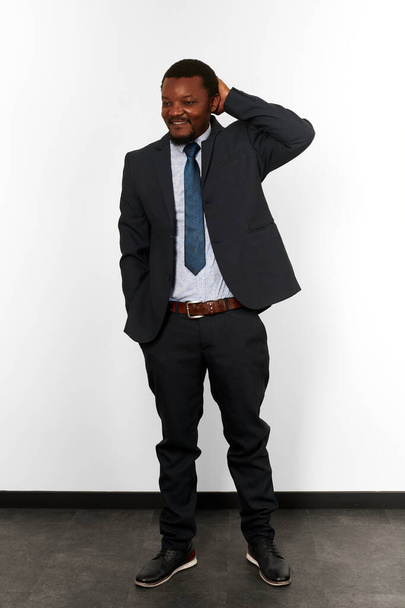 Confused smiling african american black man in business suit full size portrait white wall background. Happy puzzled black man executive businessman, chief executive officer scratching his head - Fotoğraf, Görsel
