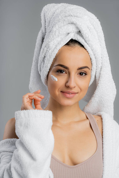 Pretty woman with towel on head and cream on face isolated on grey  - Zdjęcie, obraz