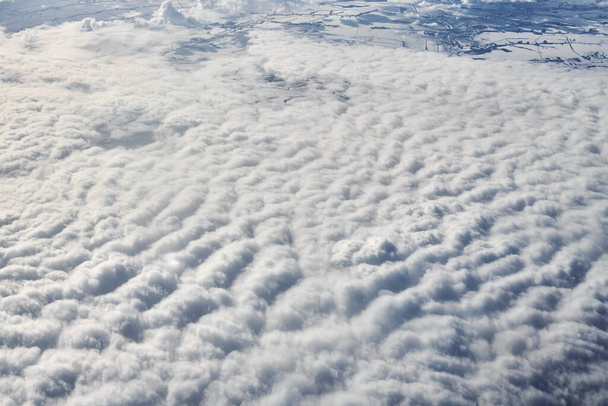 Over clouds top view from aircraft window, thick white blue clouds looks like soft foam, overcast with fresh frosty air. Beautiful cloudy sky view to troposphere, heavy cloudiness - Foto, Imagen