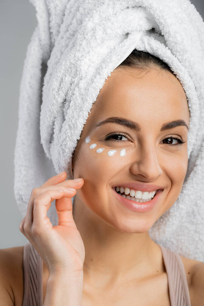 Positive woman with towel on head and cream on face looking at camera isolated on grey  - Foto, Imagem