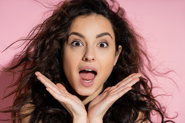Portrait of shocked curly woman looking at camera on pink background  - Foto, afbeelding