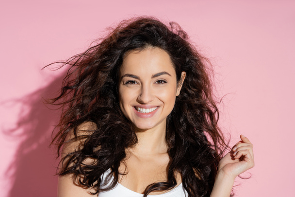 Portrait of pleased curly woman looking at camera on pink background  - Foto, Imagen