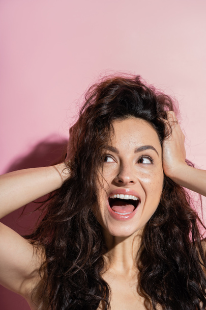 Excited brunette woman with freckled looking away on pink background  - 写真・画像