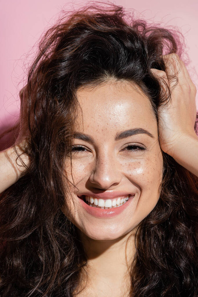 Portrait of positive woman with freckles touching hair on pink background  - Φωτογραφία, εικόνα
