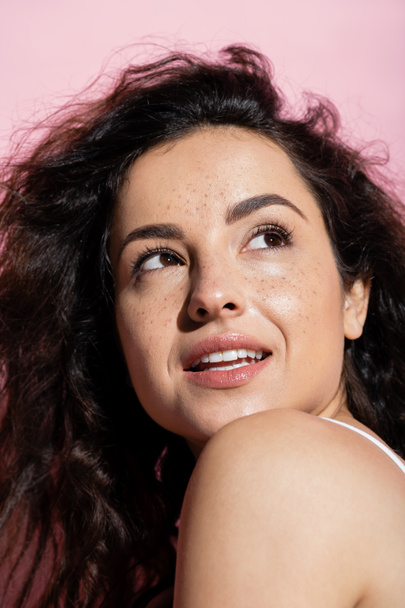 Portrait of curly and freckled woman looking away on pink background  - Photo, image