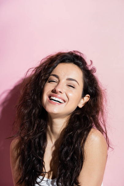 Positive young woman with curly hair looking at camera on pink background  - Foto, imagen