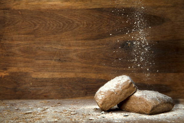 fresh baked whole grain bread on wooden background with falling flour and copy space close up - Foto, Imagen