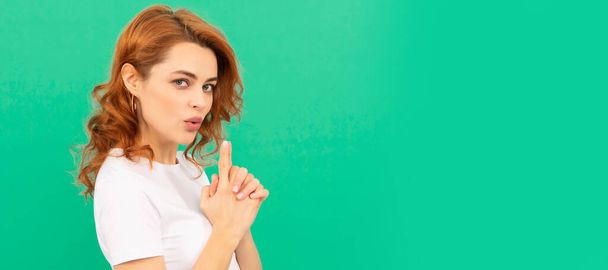 serious confident redhead girl with curly hair with gun gesture on blue background, confidence. Woman isolated face portrait, banner with copy space - Foto, Imagen