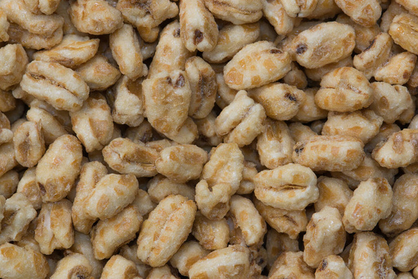 Dry honey puffed wheat cereal pieces scattered loosely directly above. Breakfast foods textured background, full frame. - Photo, image