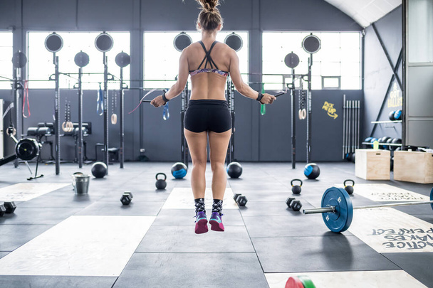 Вид ззаду молода атлетична жінка в приміщенні спортзал стрибає мотузка фітнес, тренування, спортивна концепція
 - Фото, зображення