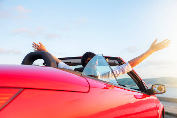海の水の背景にオープン屋根と赤い車の中で女性。旅行、自由と休日の概念. - 写真・画像