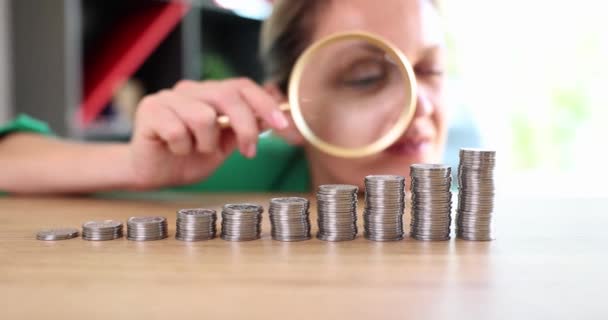 Businesswoman looking through magnifying glass at coins in ascending order 4k movie slow motion. Business earning strategy concept  - Séquence, vidéo