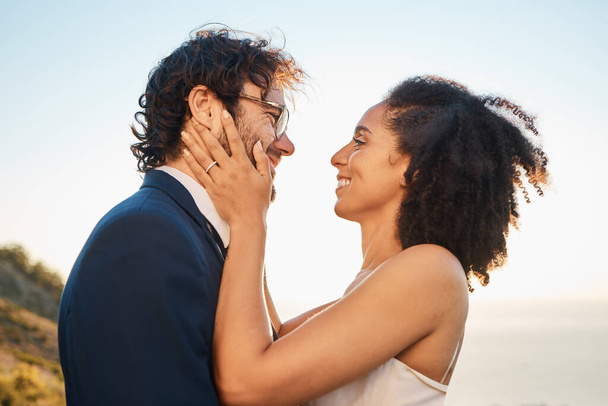 Wedding, love and interracial couple on mountain for marriage ceremony, commitment and celebration by sea. Romantic holiday, happy and bride and groom bonding, hug and smile by ocean with sunset. - Foto, afbeelding