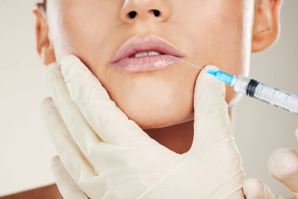 Skincare, mouth and collagen, woman with injection in lips from healthcare professional, anti aging treatment in studio. Beauty, needle and model with facial lip filler syringe on white background - Foto, immagini