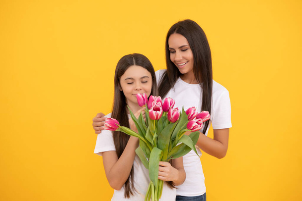 счастливая мать и дочь с букетом тюльпанов на желтом фоне. - Фото, изображение