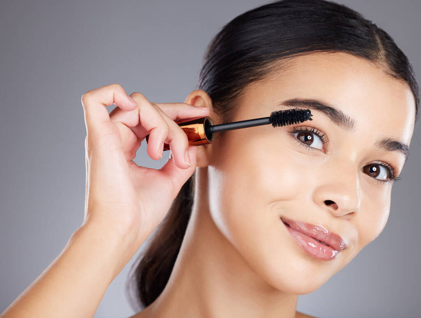 Portrait, eyelash and brush for makeup, mascara and beauty with girl with grey studio background. Face, eyes and salon equipment for grooming routine, wellness and confidence with brows and cosmetics. - Foto, imagen