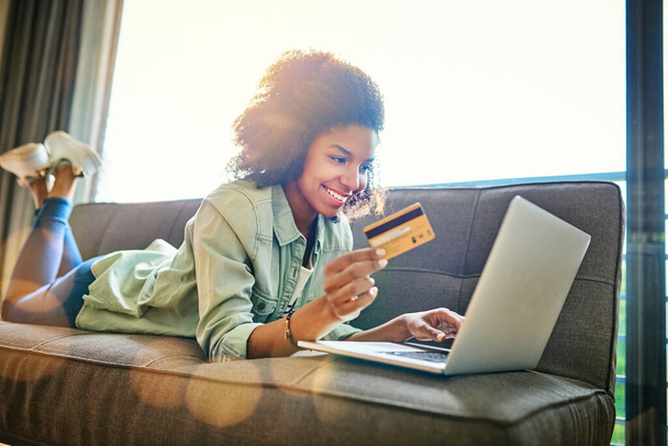 Paying the bills has never been easier. a cheerful young woman doing online shopping while lying on a couch at home during the day - Foto, imagen