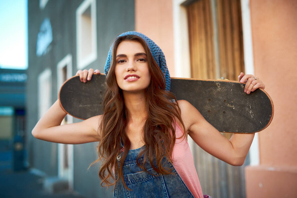 What a nice day to go out on the board. Portrait of an attractive young female skater holding a skateboard behind her back outside during the day - Foto, imagen