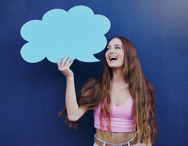 Happy woman holding a speech bubble with mockup space standing by a blue wall with a sign. Gen z, happiness and young female with a chat board with mock up or copy space for marketing or advertising - Photo, Image