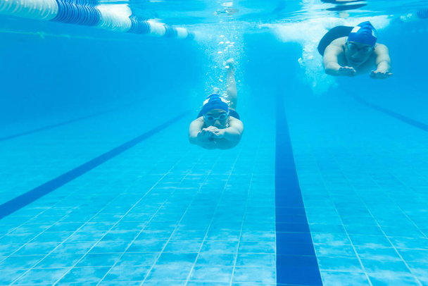 hispanic young men teenagers swimmers, athlete wearing cap in a swimming underwater training at the Pool in Mexico Latin America - Foto, Imagem