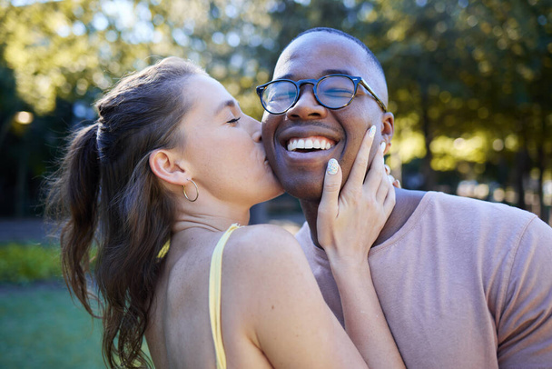 Woman kiss man, happiness and date in park, outdoor in nature with love and commitment in interracial relationship. Trust, support and happy couple, content with smile on face and fresh air. - Фото, изображение