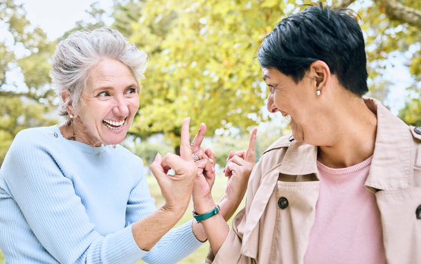 Elderly, women and middle finger at the park for fun, humor and silly while laughing together. Mature, friends and females with hand, emoji and gesture, playful and happy, smile and bonding in nature. - Foto, immagini