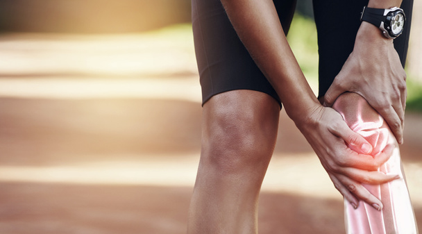 Kädet, polvi ja vamma, kun urheilija pitelee niveltään tuskissaan onnettomuuden jälkeen juostessaan ulkona. Kunto, liikunta tai harjoittelu ja loukkaantuneen jalan kanssa kamppaileva miesurheilija. - Valokuva, kuva