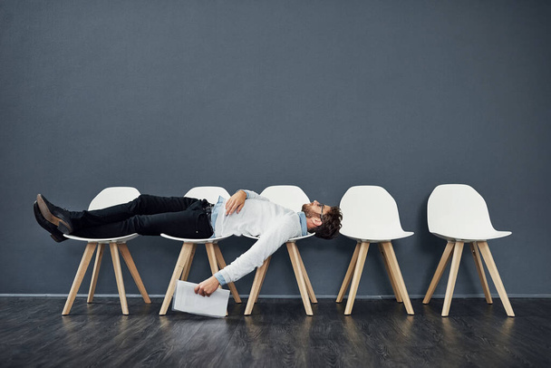 Can this wait get any longer. Full length shot of a handsome young man lying down on a row of chairs while waiting in line for a job interview - Photo, Image