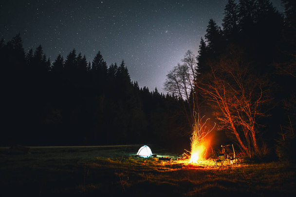 Φωτιζόμενη σκηνή και φωτιά κάτω από τον όμορφο νυχτερινό ουρανό γεμάτο αστέρια στο άγριο δάσος - Φωτογραφία, εικόνα
