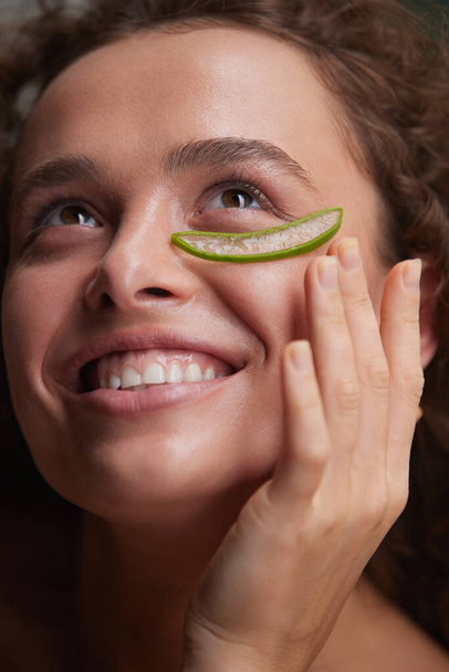 Beauty Face. Woman Holding Slices Of Fresh Juicy Aloe Vera Leaf At Her Face. Tender Brunette With Naked Shoulder, Natural Makeup And Perfect Skin. Organic Cosmetic For SPA Therapy  - 写真・画像