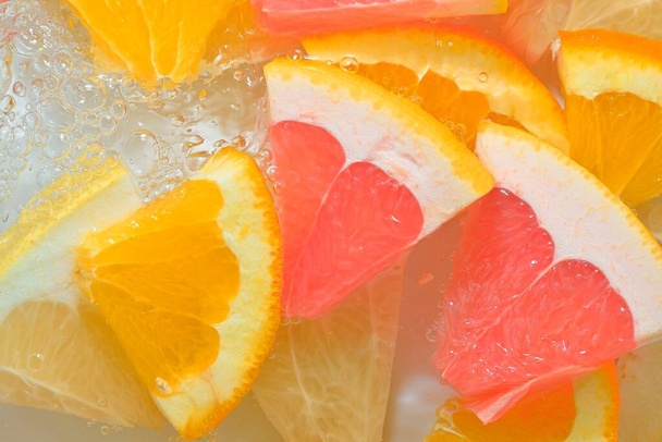Fresh slices of juicy grapefruit, orange fruit and honey pomelo on white background. Pieces of grapefruit, orange fruit and honey pomelo in sparkling water on white background, closeup. Horizontal image. - Foto, Imagem