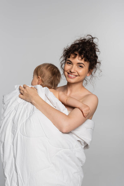 積極的な母親と幼児の女の子は灰色で隔離されたduvetに覆われています  - 写真・画像