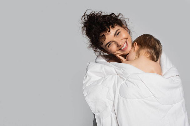 happy mother and toddler daughter covered in white blanket isolated on grey  - Valokuva, kuva