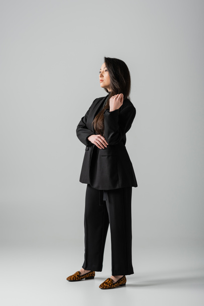 full length of young asian businesswoman in black suit standing on grey  - 写真・画像