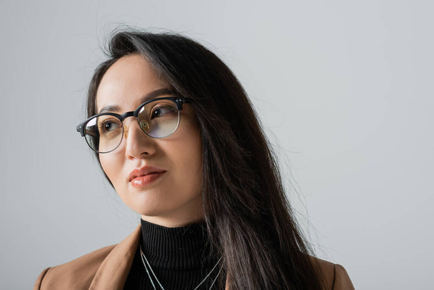 portrait of brunette asian businesswoman in beige blazer and glasses looking away isolated on grey  - Photo, Image