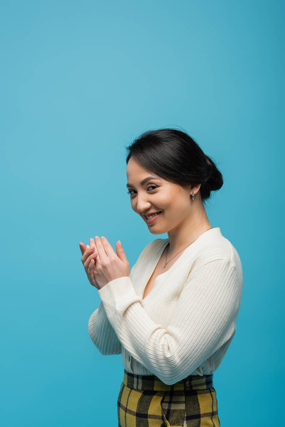Легко азіатська жінка в кардигані дивиться на камеру ізольовано на синьому
  - Фото, зображення