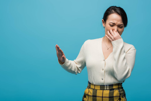Disgusted asian woman pinching nose and showing no sign isolated on blue  - Foto, Bild