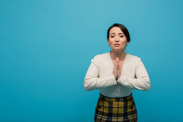 Asian woman in cardigan showing praying hands gesture isolated on blue  - Photo, image