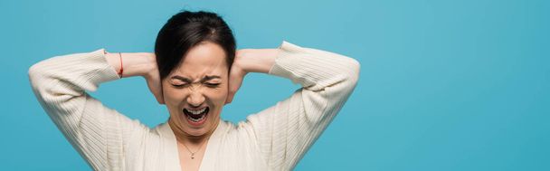 Aggressive asian woman screaming and covering ears isolated on blue, banner  - Foto, Imagem