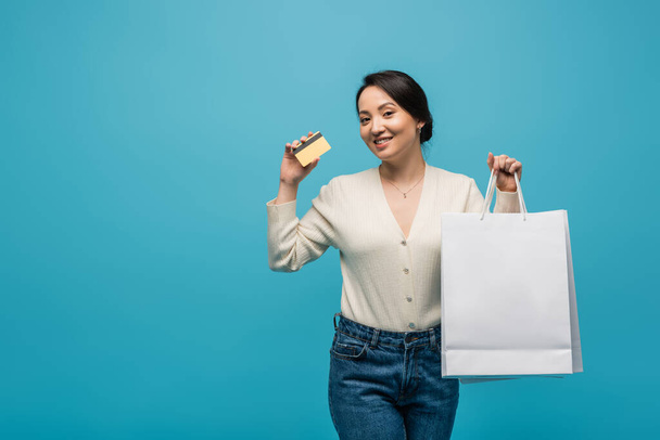 Young asian customer holding shopping bags and credit card isolated on blue  - Fotoğraf, Görsel