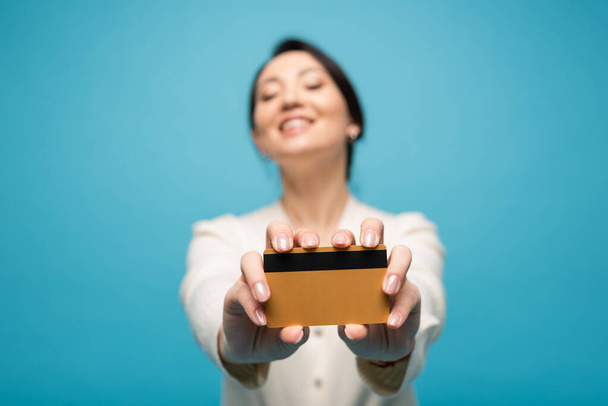Blurred asian woman holding credit card isolated on blue  - Fotografie, Obrázek