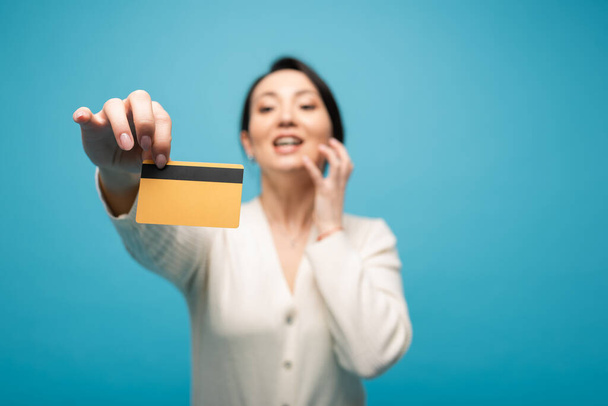 Blurred asian model showing credit card isolated on blue with copy space  - Φωτογραφία, εικόνα