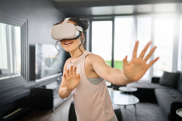 VR, metaverse and futuristic with a woman in the living room of her home using a headset to access a 3d game. Technology, virtual reality and gaming with a female gamer using ai to play online games. - Foto, imagen
